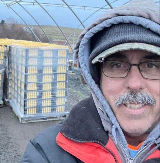 Man in winter clothing standing outdoors near a stack of wooden pallets.