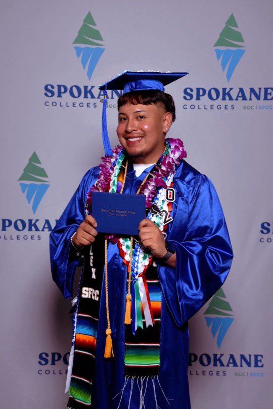 Graduate in blue cap and gown, smiling proudly.